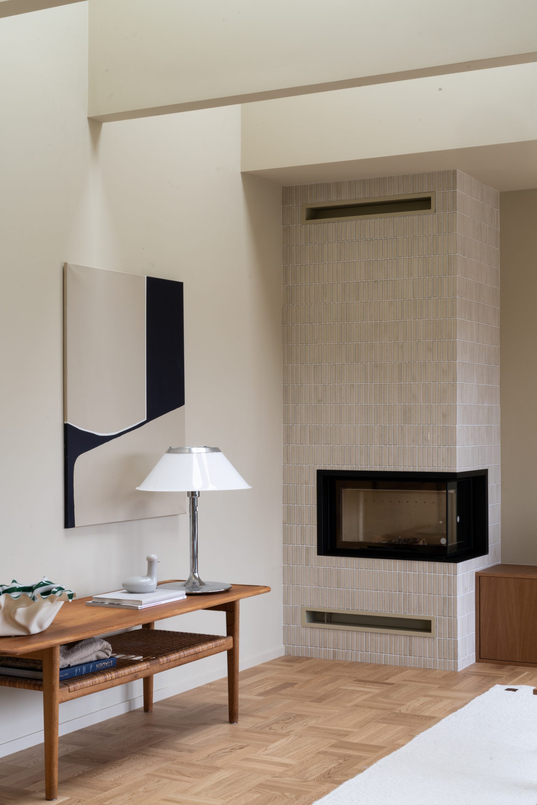 Moderne stue med minimalistisk interiør, inneholder et flislagt ildsted, et trebord med en hvit lampe og abstrakt kunst på veggen, Vegger og tak malt i gulbeige med Jotun 11173 Humble Yellow