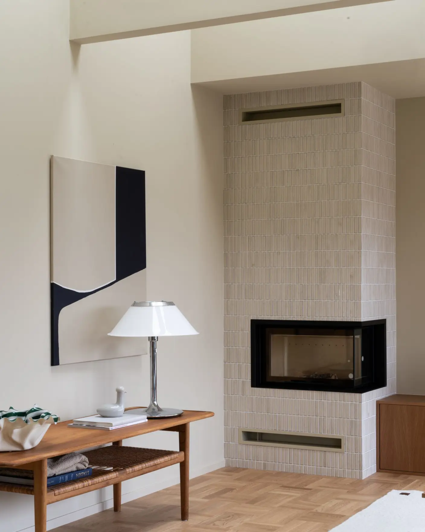 Moderne stue med minimalistisk interiør, inneholder et flislagt ildsted, et trebord med en hvit lampe og abstrakt kunst på veggen, Vegger og tak malt i gulbeige med Jotun 11173 Humble Yellow