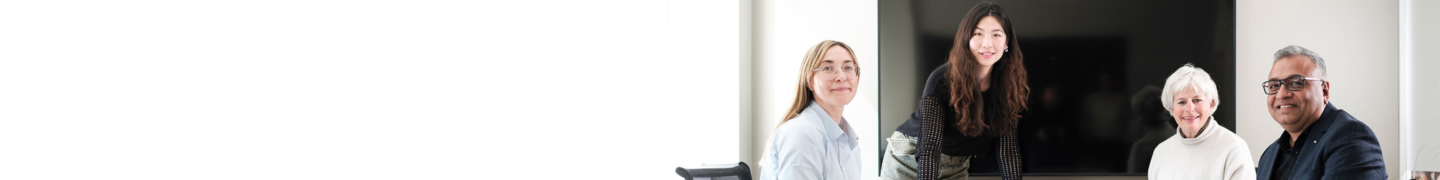 Fyra personer framför en stor skärm i ett kontorsmiljö, leende och samlade för ett möte