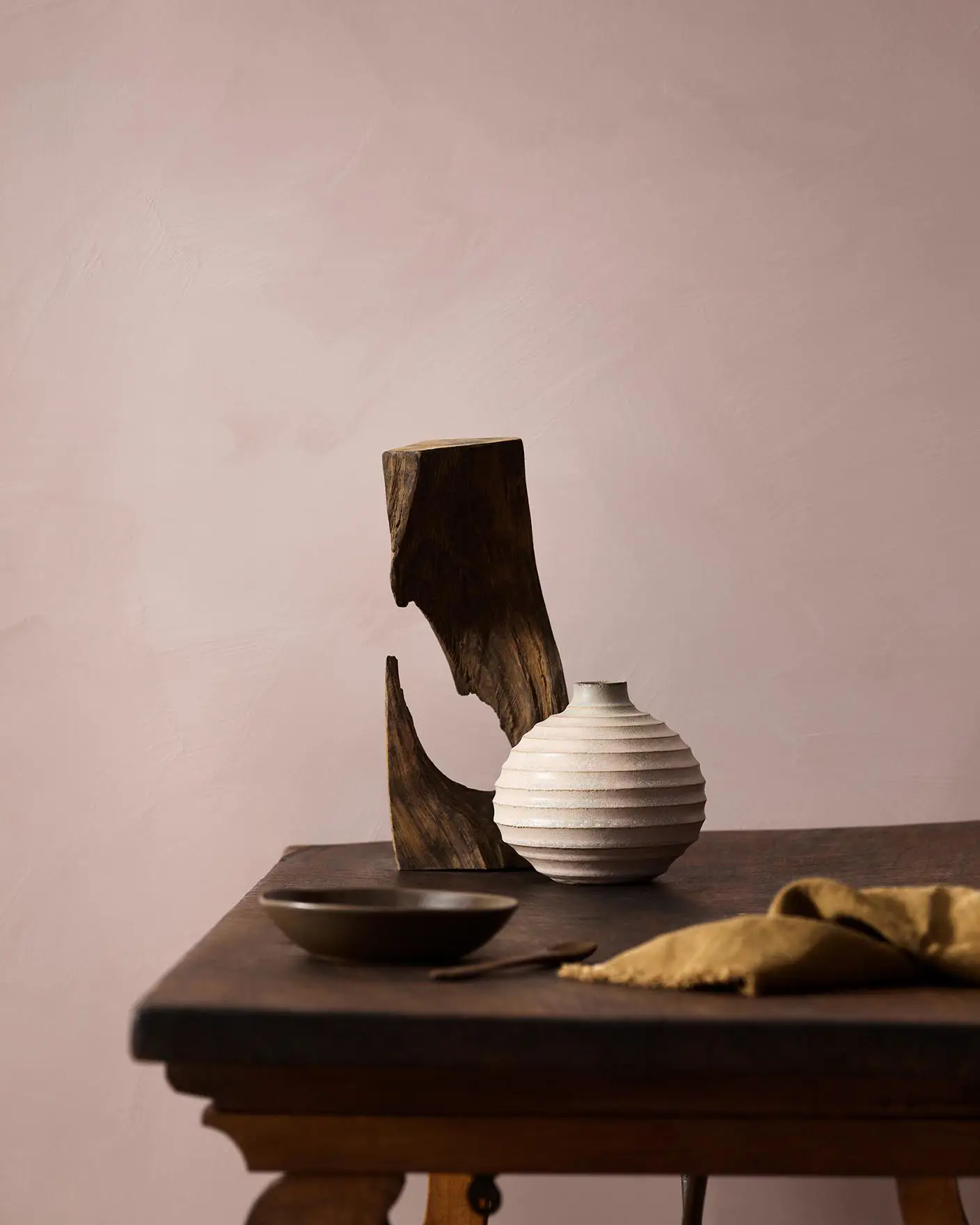 Wooden table with a ceramic vase, sculpted wood, and a dark bowl against a muted pink background painted with LADY Design Touch of Suede in the colour 20054 Silky Pink from Jotun.