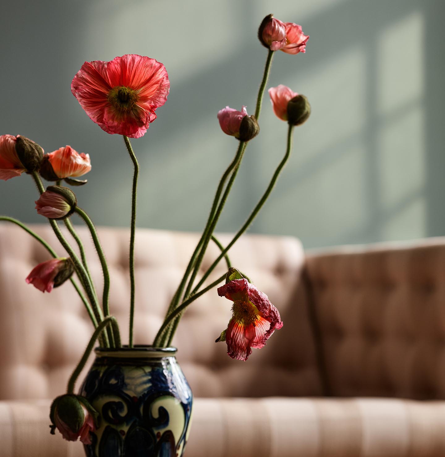 Vase with pink and red flowers on a table in front of a beige sofa. Background wall in the muted green colour Jotun 7613 Northern Mystic.