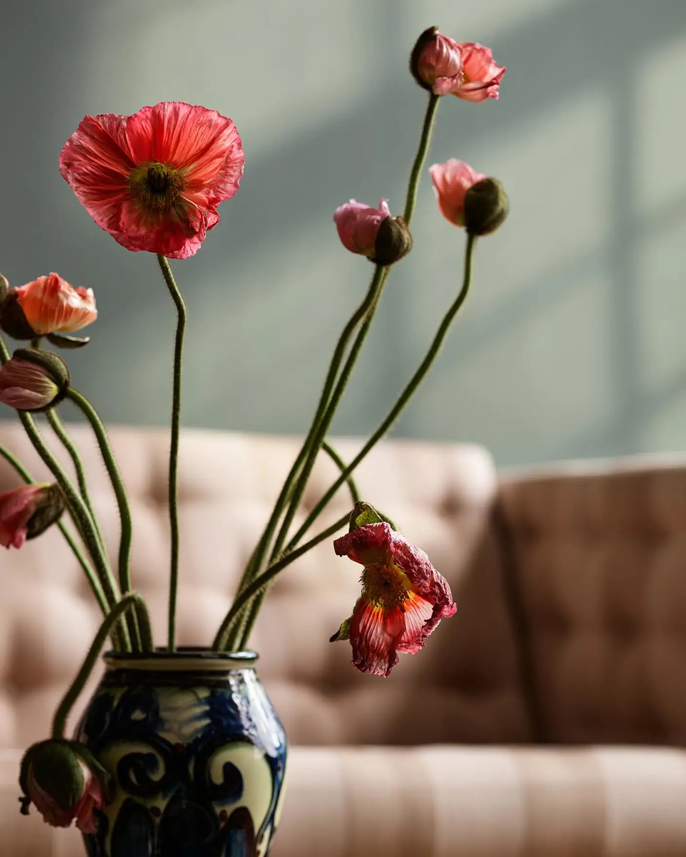 Vase with pink and red flowers on a table in front of a beige sofa. Background wall in the muted green colour Jotun 7613 Northern Mystic.