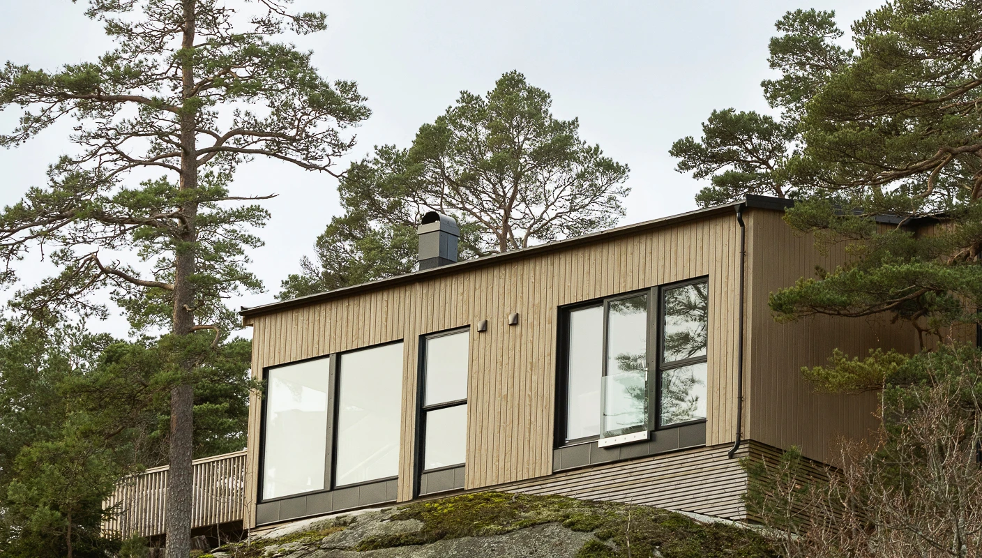 Moderne funkisshytte omringet av trær og fjell