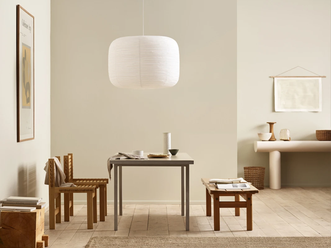 Moderne spisestue med bord med en stor, hvit taklampe over, to stoler og benk i mørkt treverk, mot beige vegger malt i Jotun 12308 Unbleached