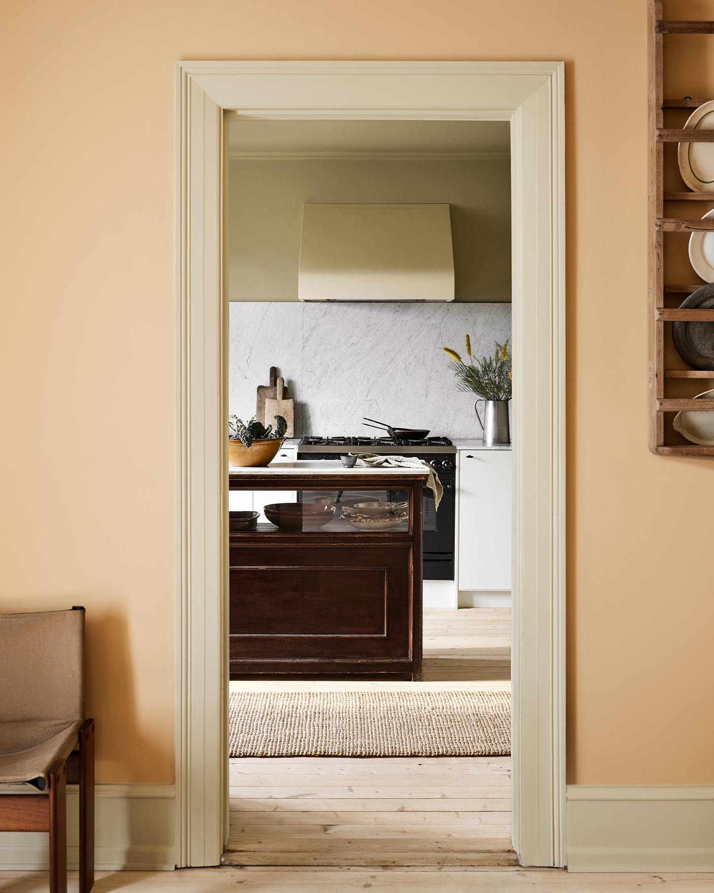 Kitchen viewed through a doorway. The wall in front is painted in the pale, ochre yellow colour 11202 Mild Ochre from Jotun. 