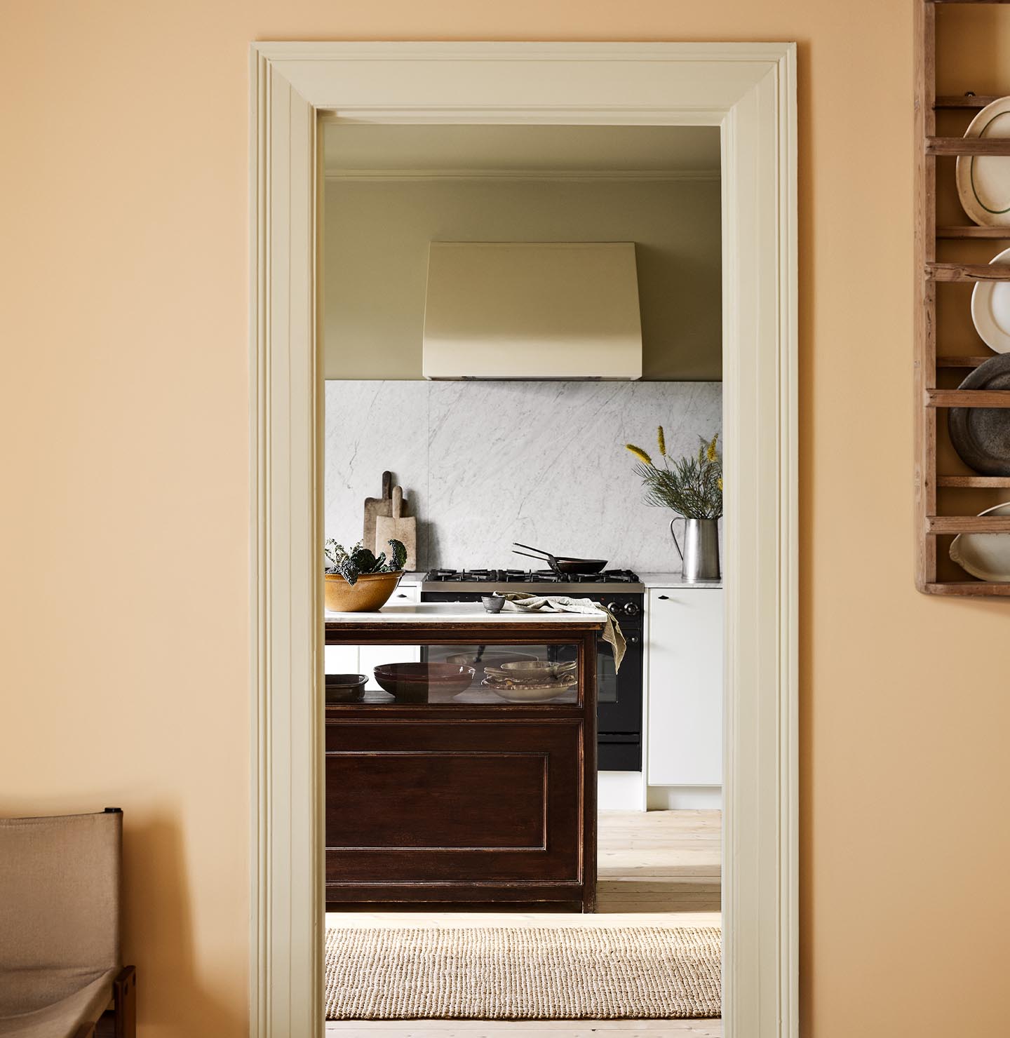 Kitchen viewed through a doorway. The wall in front is painted in the pale, ochre yellow colour 11202 Mild Ochre from Jotun. 