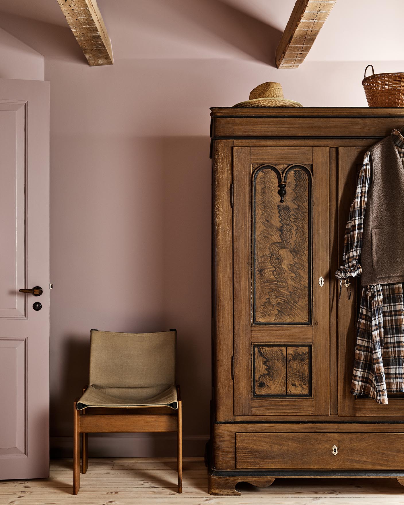 Bedroom with a wooden wardrobe and chair against a muted pink wall painted with Jotun's colour 20054 Silky Pink.