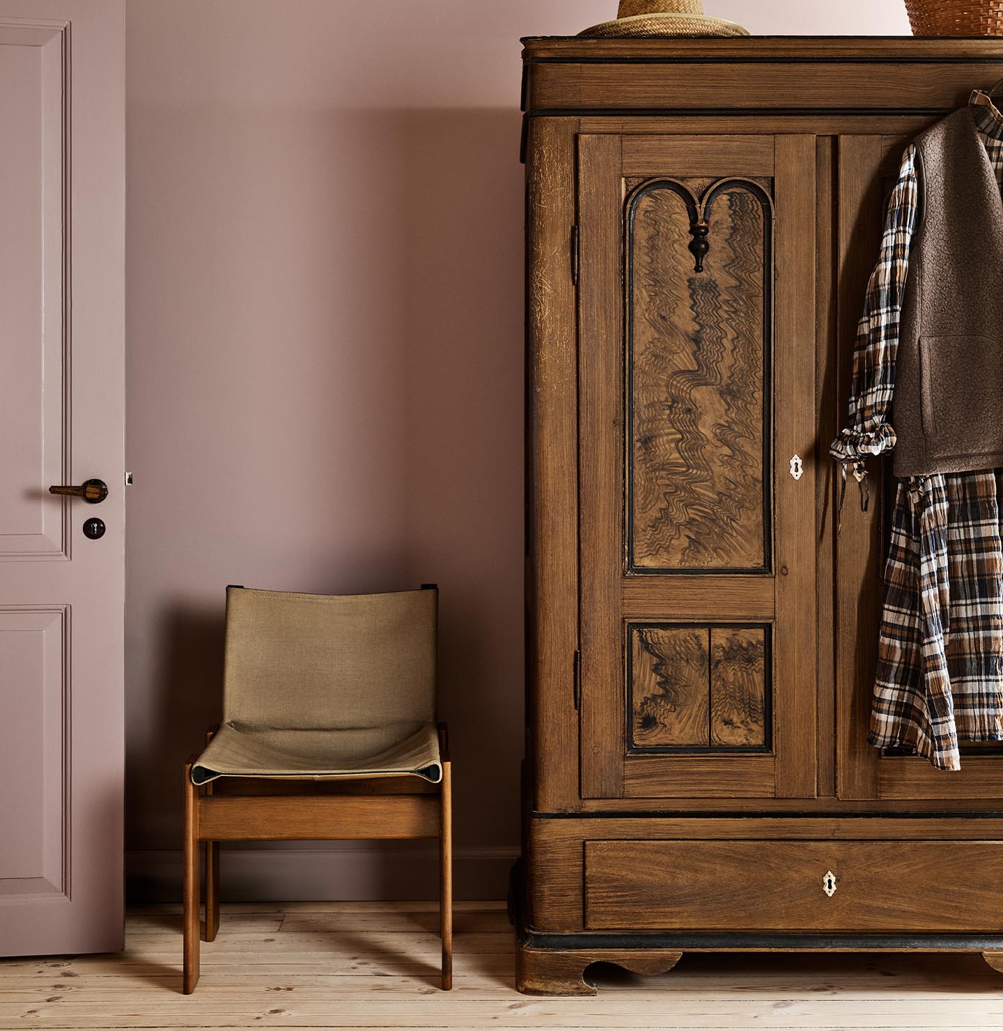 Bedroom with a wooden wardrobe and chair against a muted pink wall painted with Jotun's colour 20054 Silky Pink.
