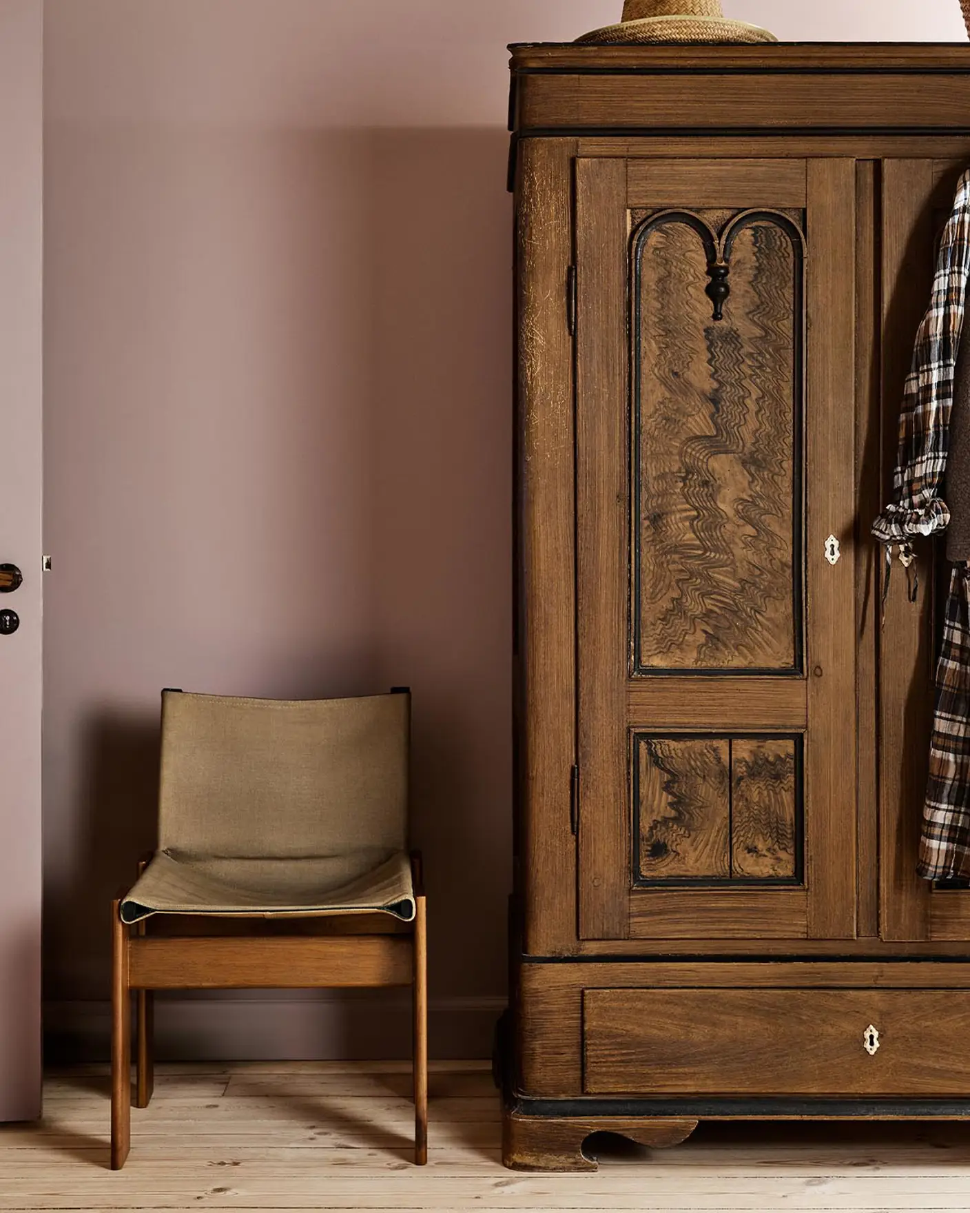 Bedroom with a wooden wardrobe and chair against a muted pink wall painted with Jotun's colour 20054 Silky Pink.