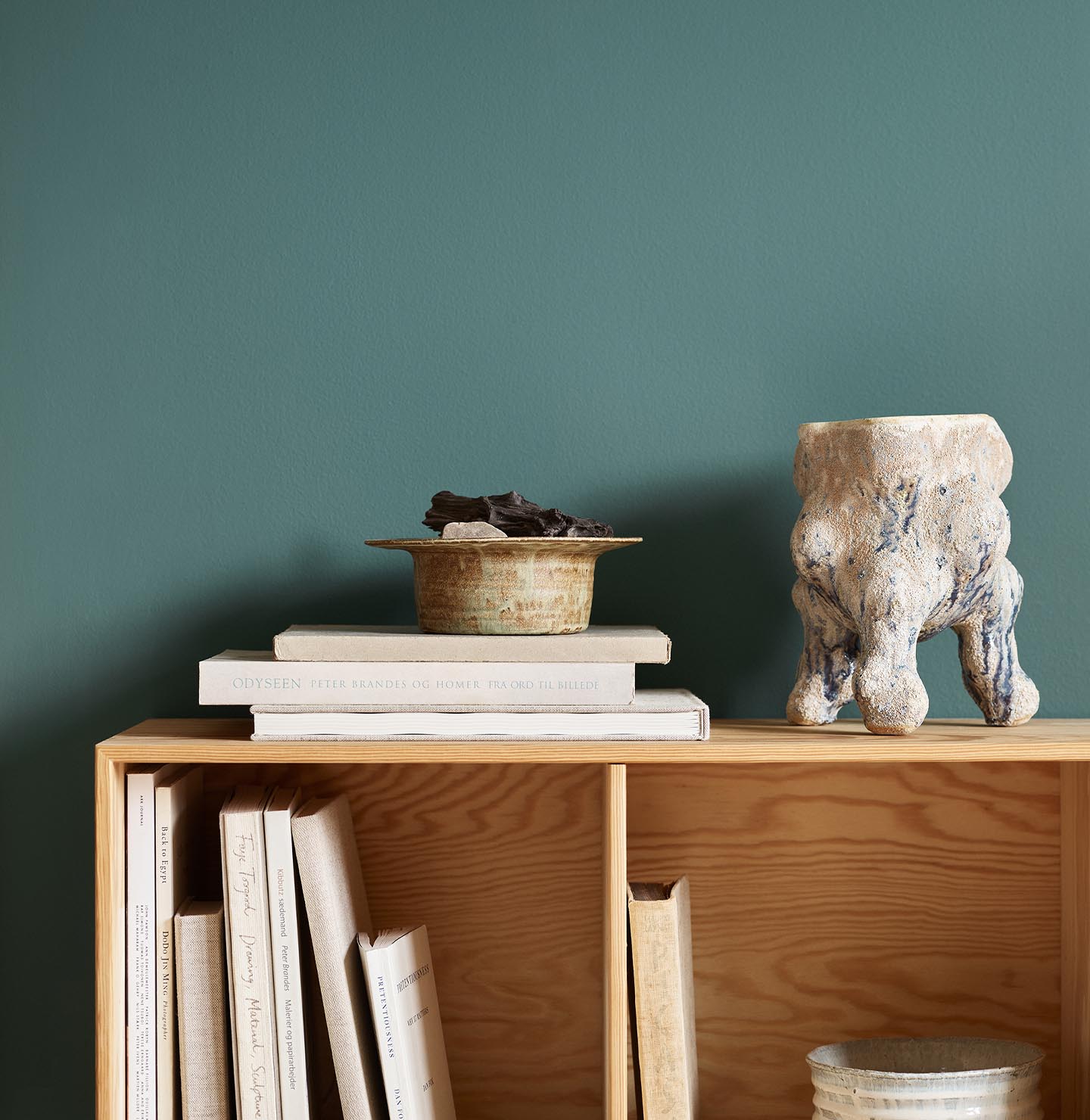 Bookshelf with stacked books, bowl, and ceramic sculpture against a green wall painted in the Jotun colour 6194 Wild Ivy.
