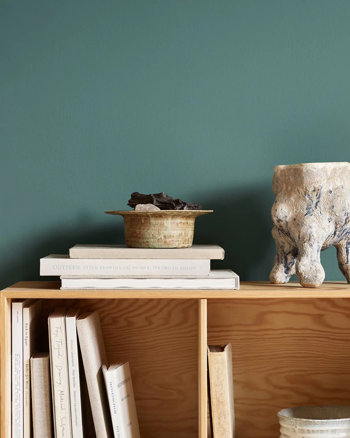 Bookshelf with stacked books, bowl, and ceramic sculpture against a green wall painted in the Jotun colour 6194 Wild Ivy.