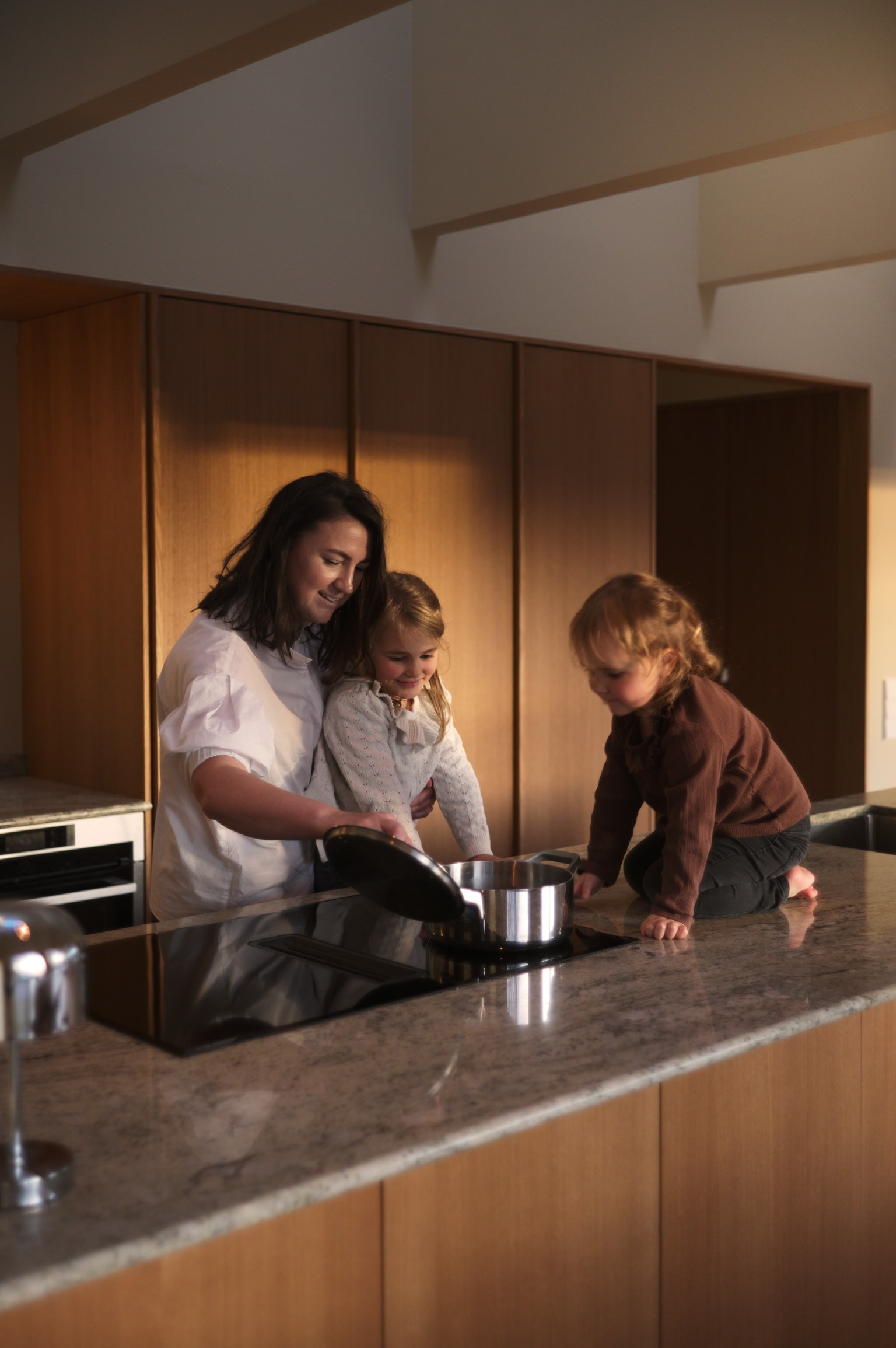 Kvinne lager mat med to barn på benken i et moderne kjøkken