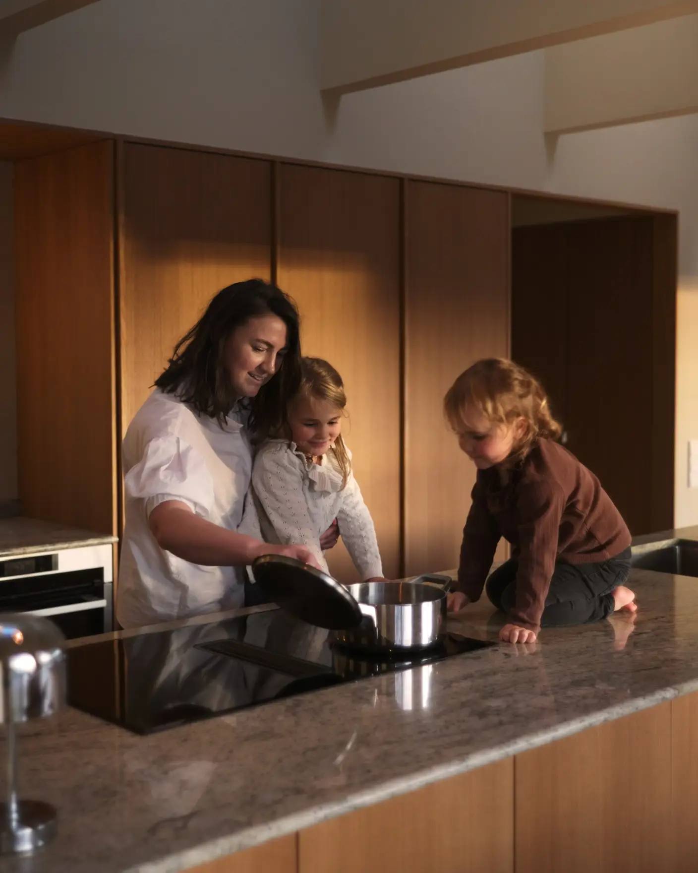 Kvinne lager mat med to barn på benken i et moderne kjøkken