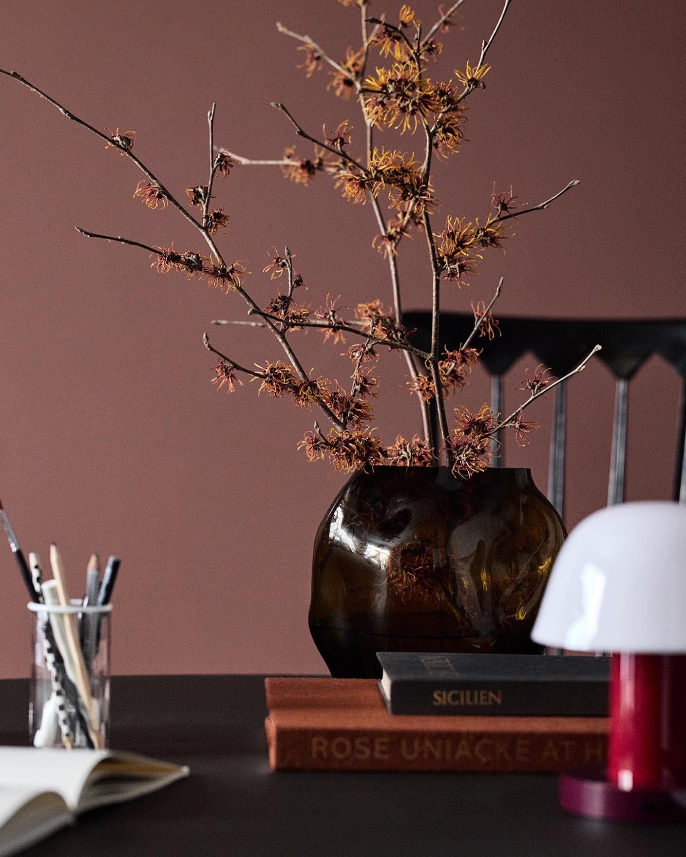 A glass vase on a table set against a deep red wall painted in the colour 2951 Sophisticated Red from Jotun.