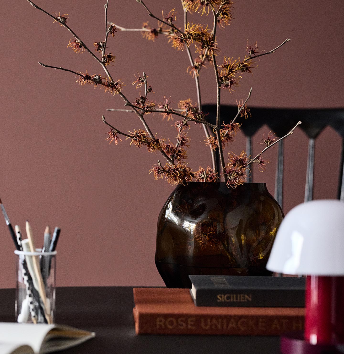 A glass vase on a table set against a deep red wall painted in the colour 2951 Sophisticated Red from Jotun.