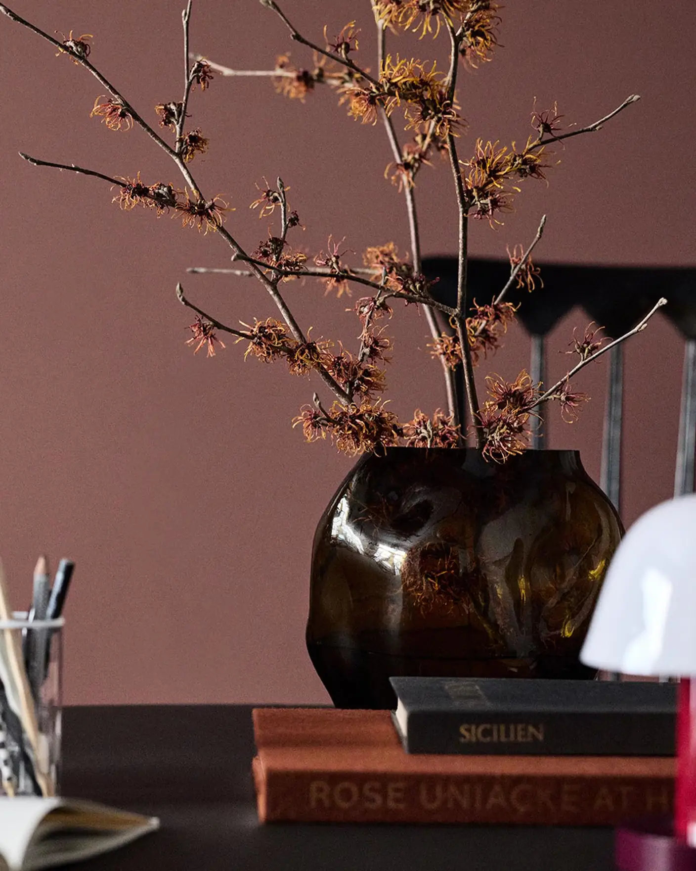 A glass vase on a table set against a deep red wall painted in the colour 2951 Sophisticated Red from Jotun.