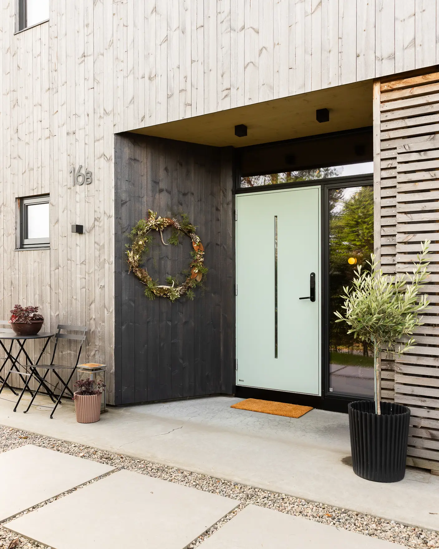 Inngangsparti oljet med vedlikeholdsoljen TREBITT WoodCare i den gråsorte fargen Muted Charcoal. Krans på veggen og grønn dør.