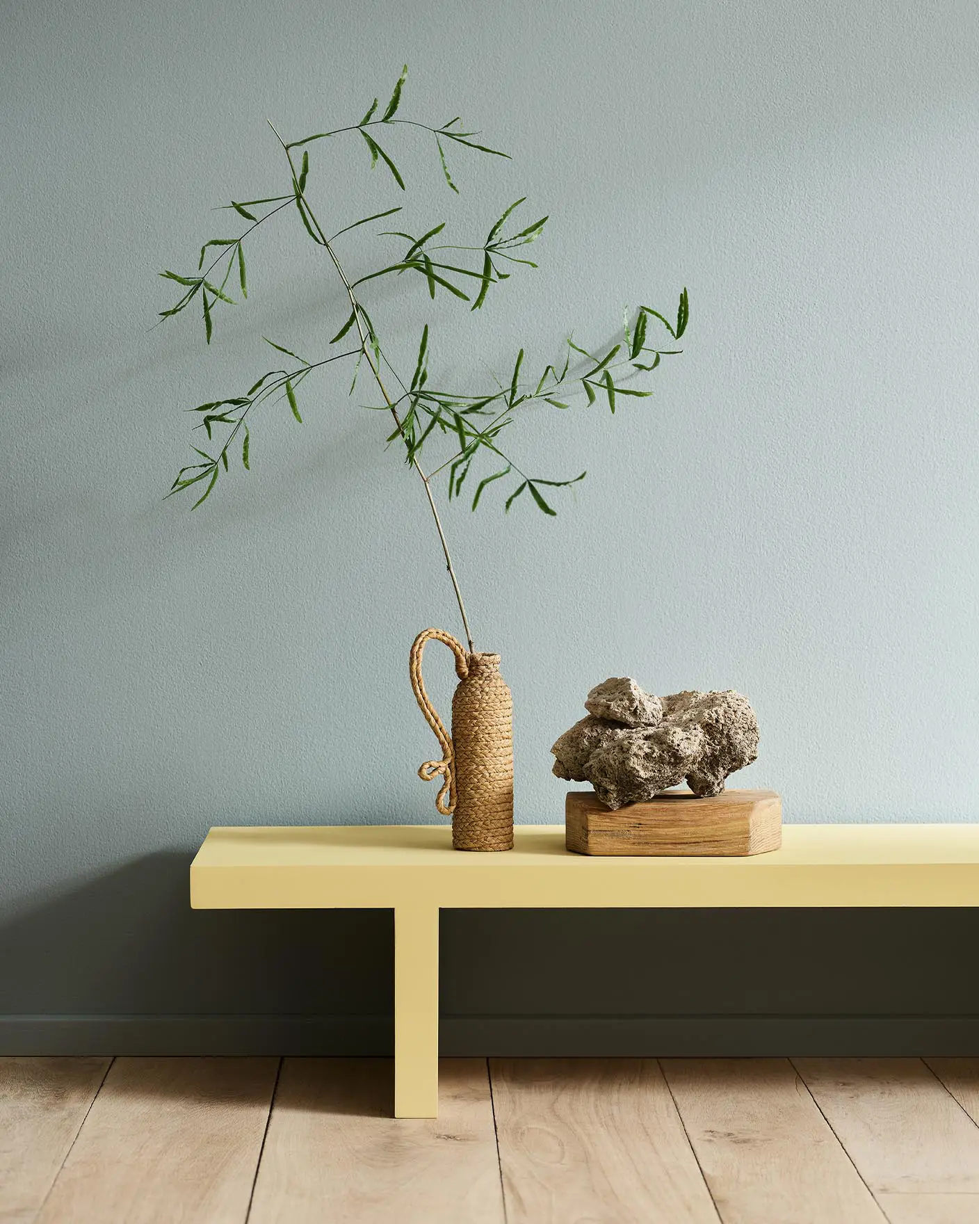 Minimalist interior with a greenish yellow bench in the colour 1965 Ginger Tea set against a muted blue wall painted with 6378 Iconic from Jotun.