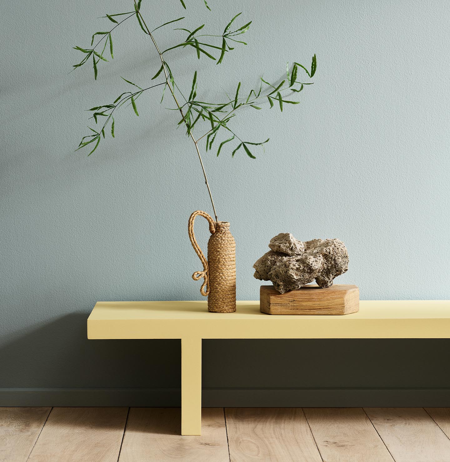 Minimalist interior with a greenish yellow bench in the colour 1965 Ginger Tea set against a muted blue wall painted with 6378 Iconic from Jotun.