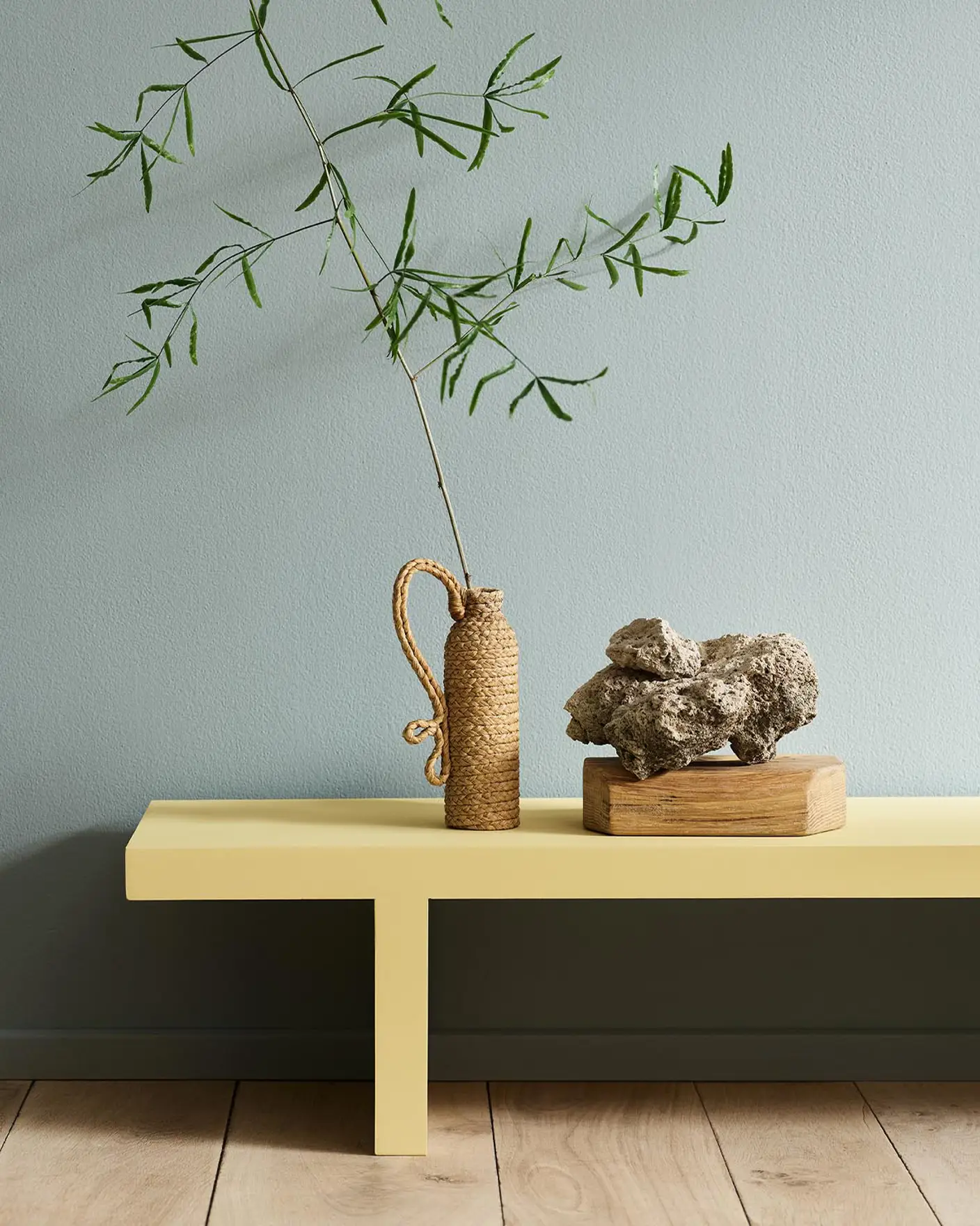 Minimalist interior with a greenish yellow bench in the colour 1965 Ginger Tea set against a muted blue wall painted with 6378 Iconic from Jotun.