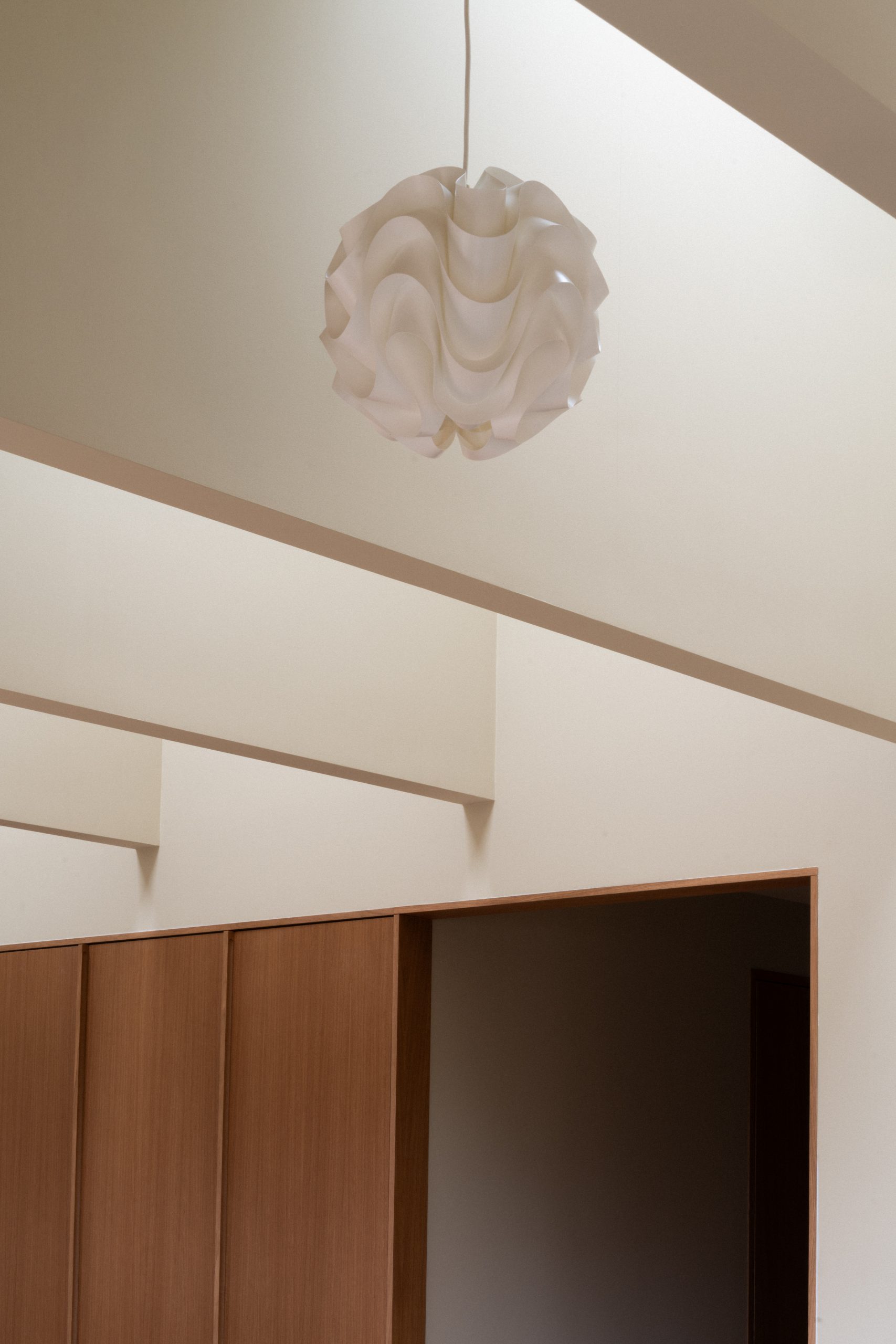 Hvitt, bølget taklampe i modernistisk interiør med lyse vegger og trepaneler