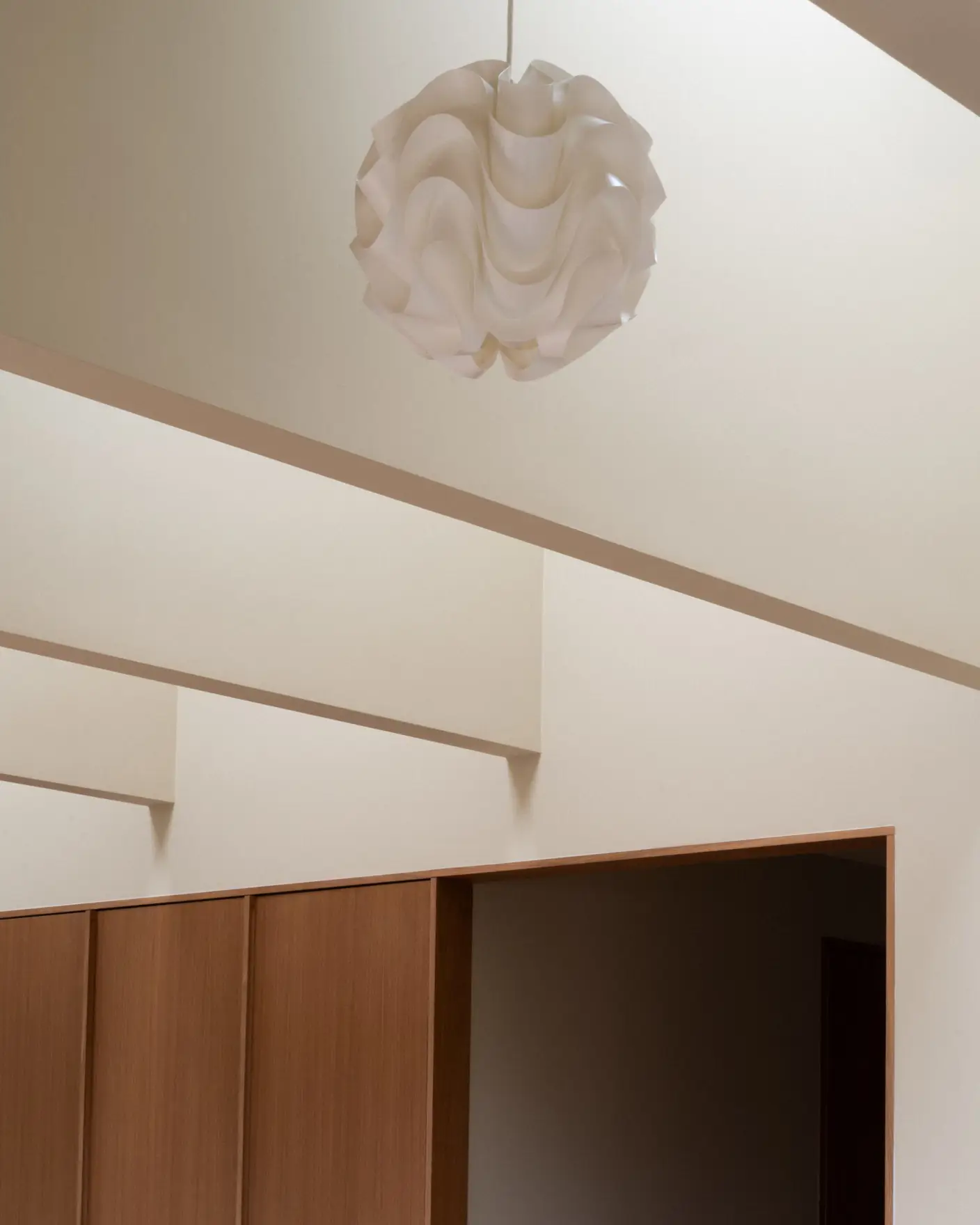 Hvitt, bølget taklampe i modernistisk interiør med lyse vegger og trepaneler