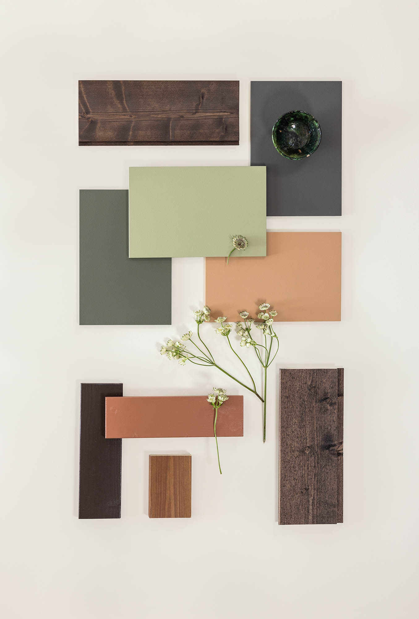 Trekonstruksjoner i forskjellige farger, inkludert grønn, brun, og terrakotta, arrangert med små hvite blomster på lys bakgrunn