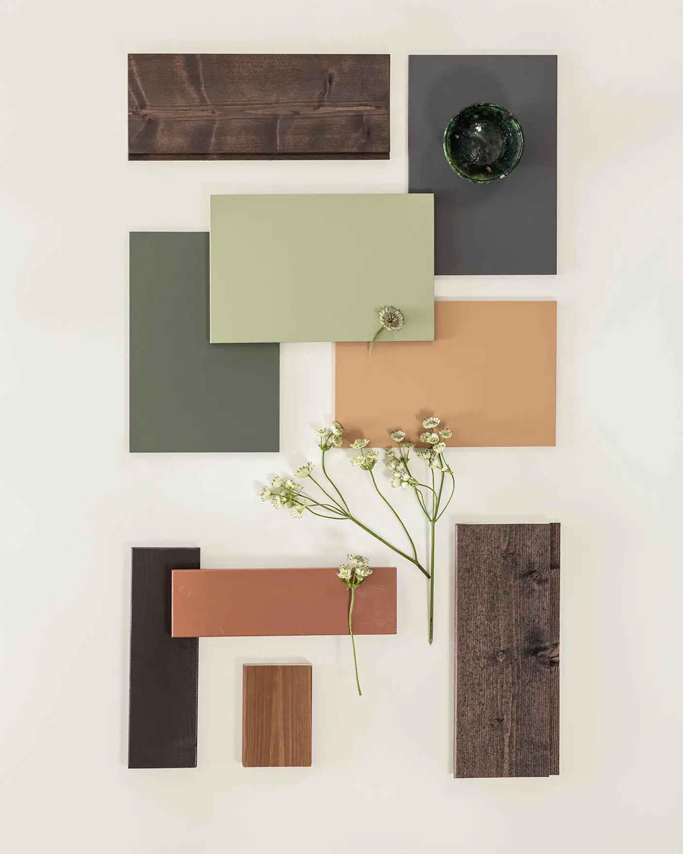 Trekonstruksjoner i forskjellige farger, inkludert grønn, brun, og terrakotta, arrangert med små hvite blomster på lys bakgrunn