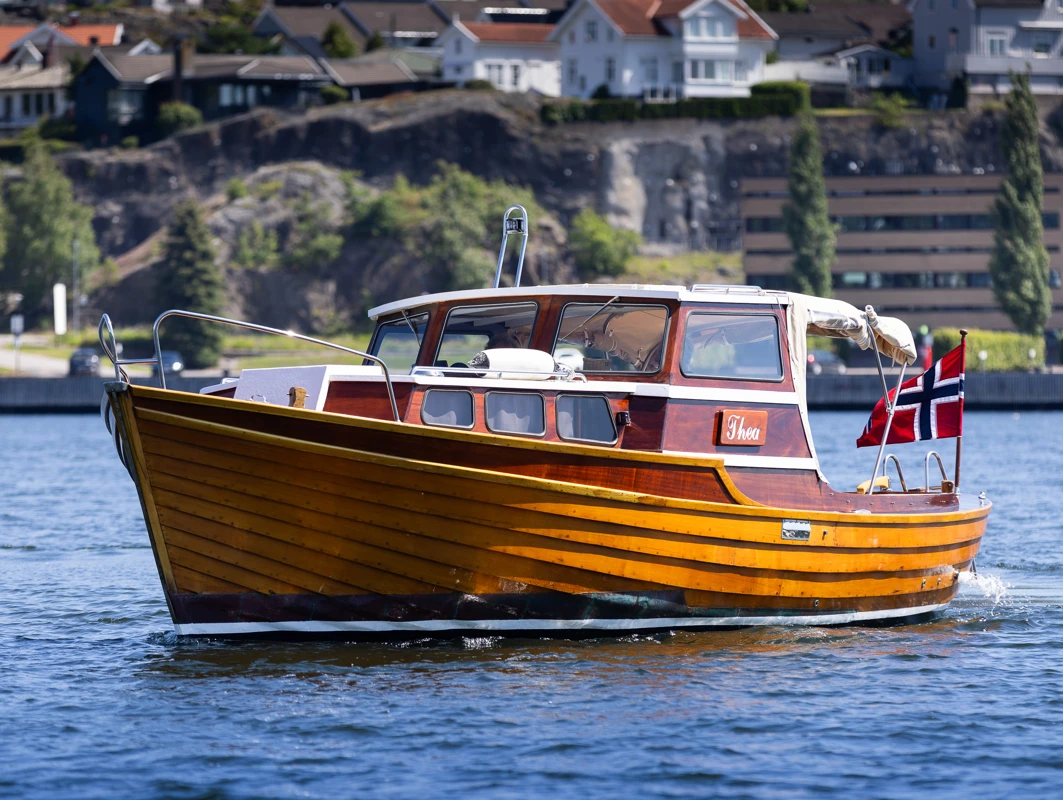 Blank og nypusset trebåt med norsk flagg, ute på fjorden en solrik sommerdag