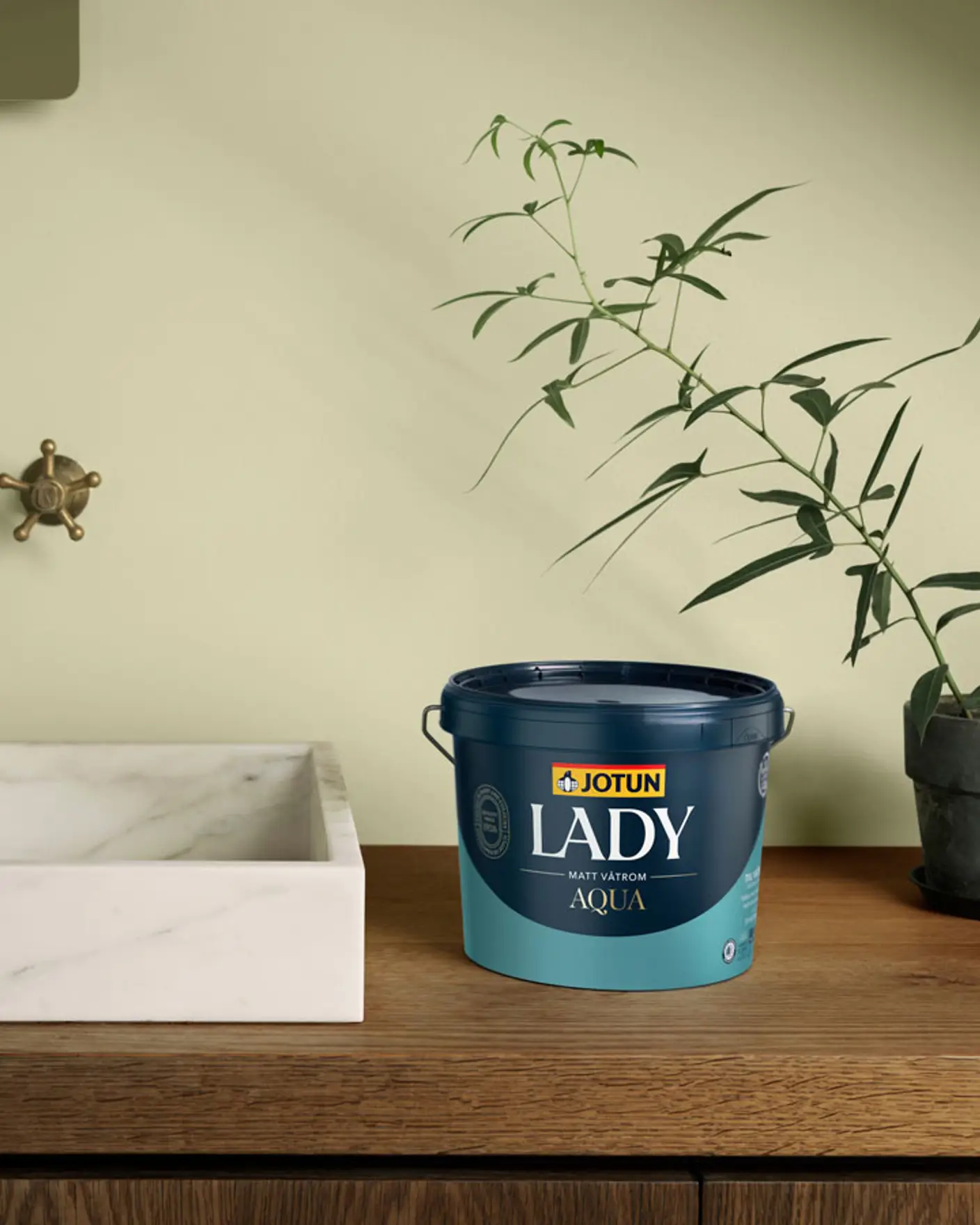 Malingbøtte merket "Jotun Lady Aqua" på en trebenk ved siden av en hvit marmorvask og potteplante i et minimalistisk miljø