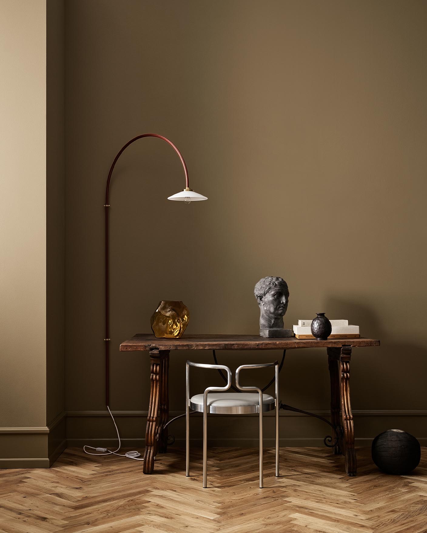 A wooden table, decor, and arched lamp against a golden brown wall in the colour 1974 Golden Walnut from Jotun.