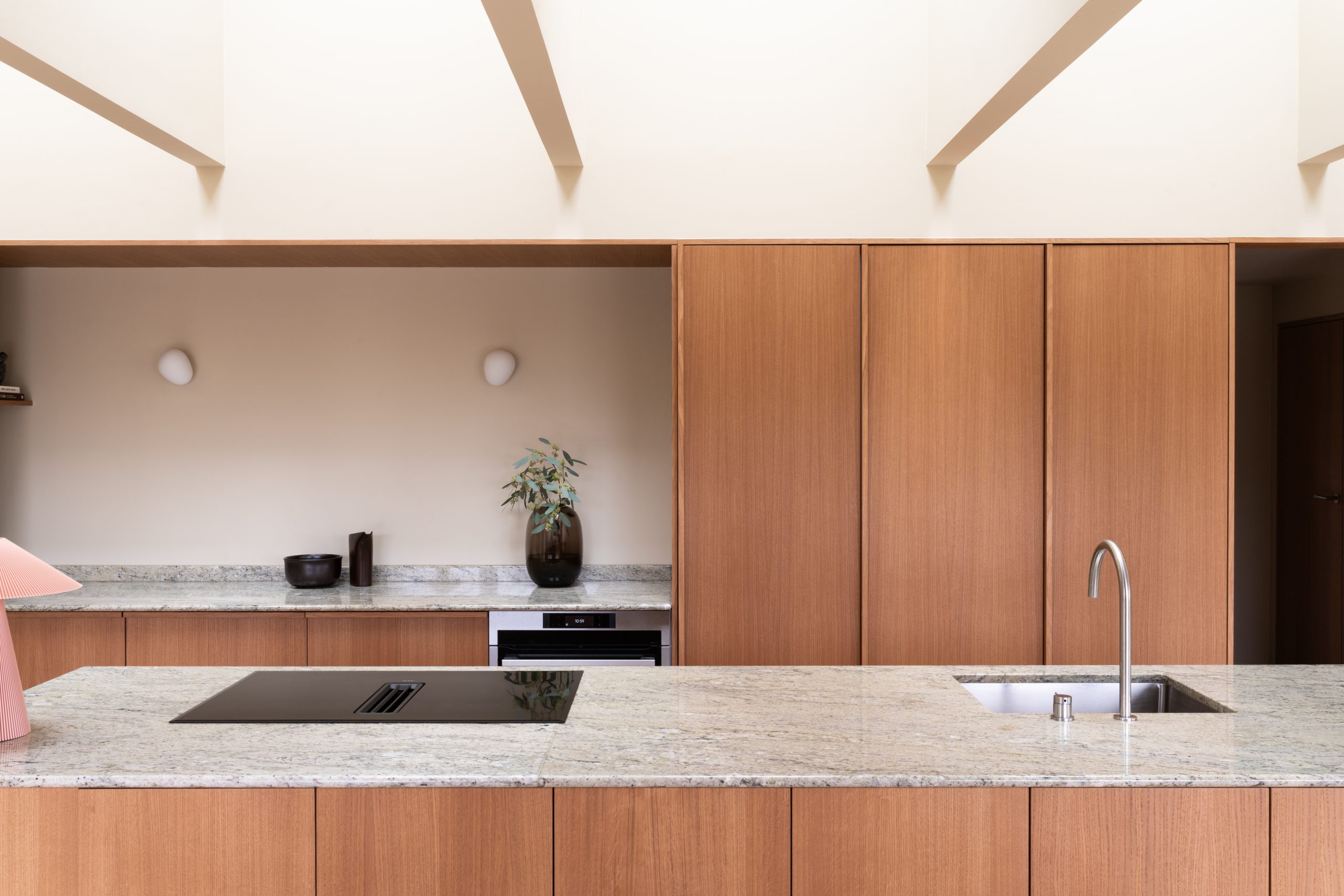 Moderne kjøkken med lysebrun treinnredning, grå benkeplate, integrert komfyr og vask, vegger malt gulbeige i Jotun 11173 Humble Yellow