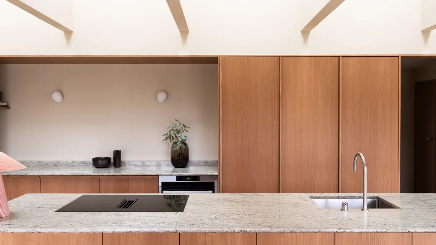 Moderne kjøkken med lysebrun treinnredning, grå benkeplate, integrert komfyr og vask, vegger malt gulbeige i Jotun 11173 Humble Yellow