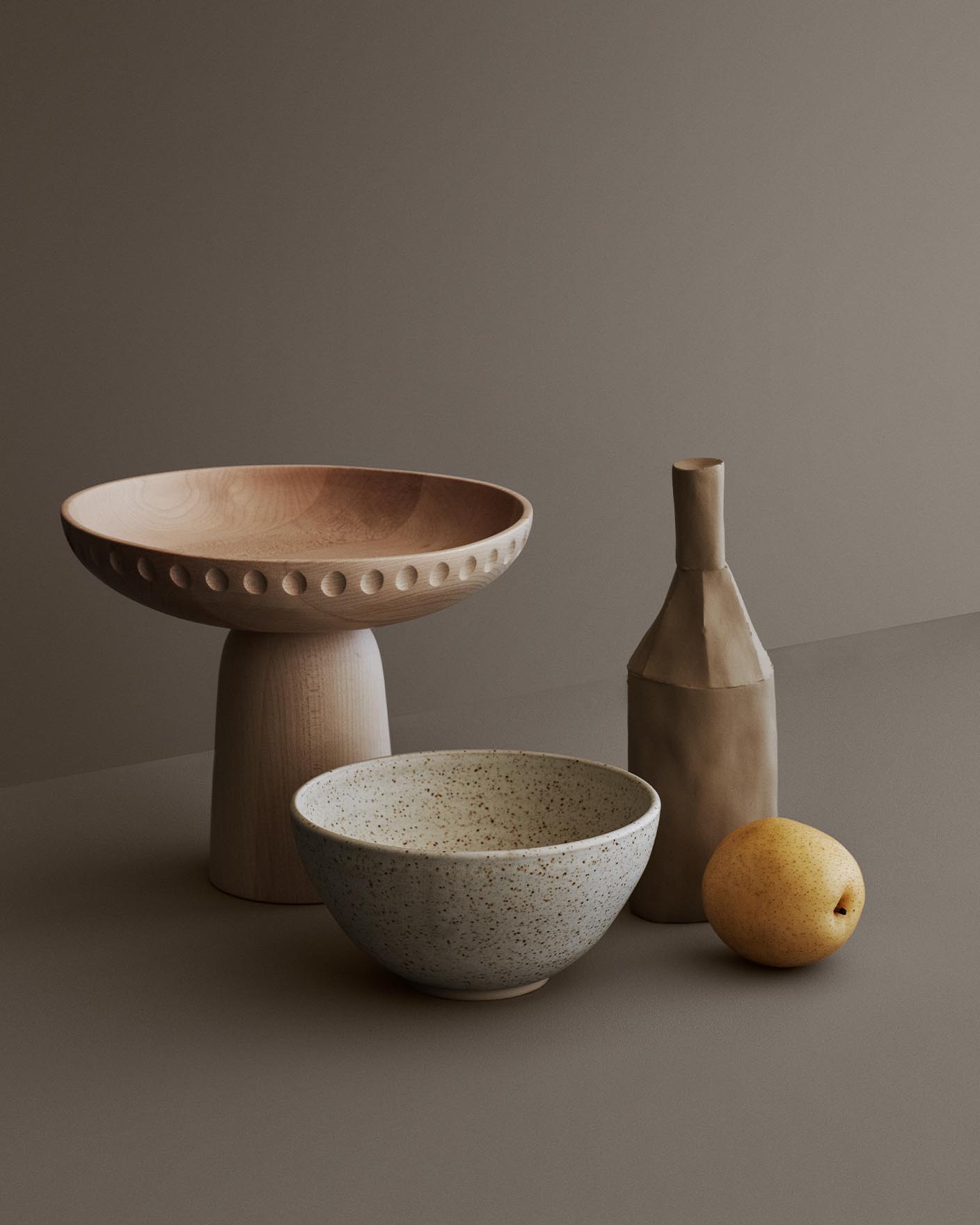 Dempede gråtoner og jordnære teksturer smelter sammen i en myk, jordnær palett med Jotun 1352 Form som bakgrunn. Den matte keramikken og det lyse treverket gir en følelse av ro og stille eleganse.