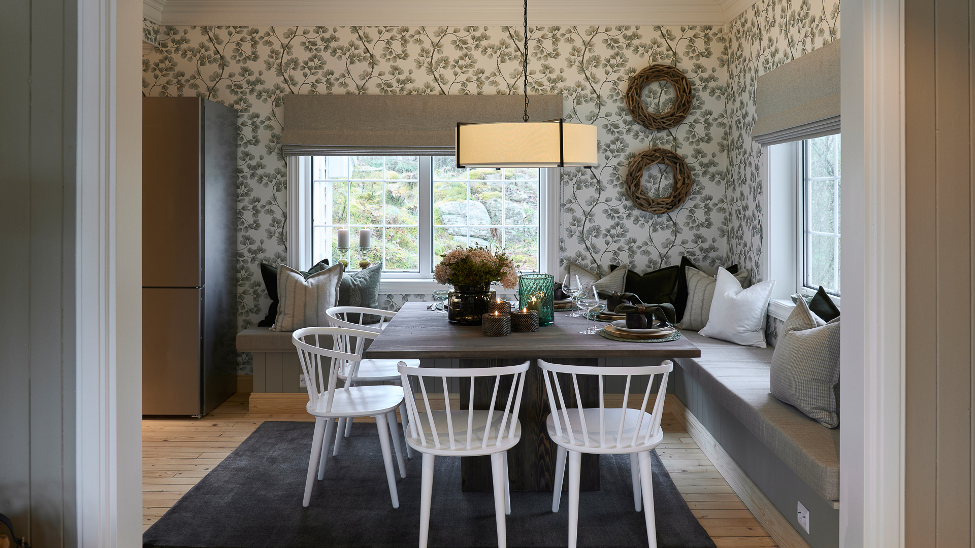 Spisestue med tapetserte vegger i grønt og hvitt, stor lampe over kvadratisk bord.