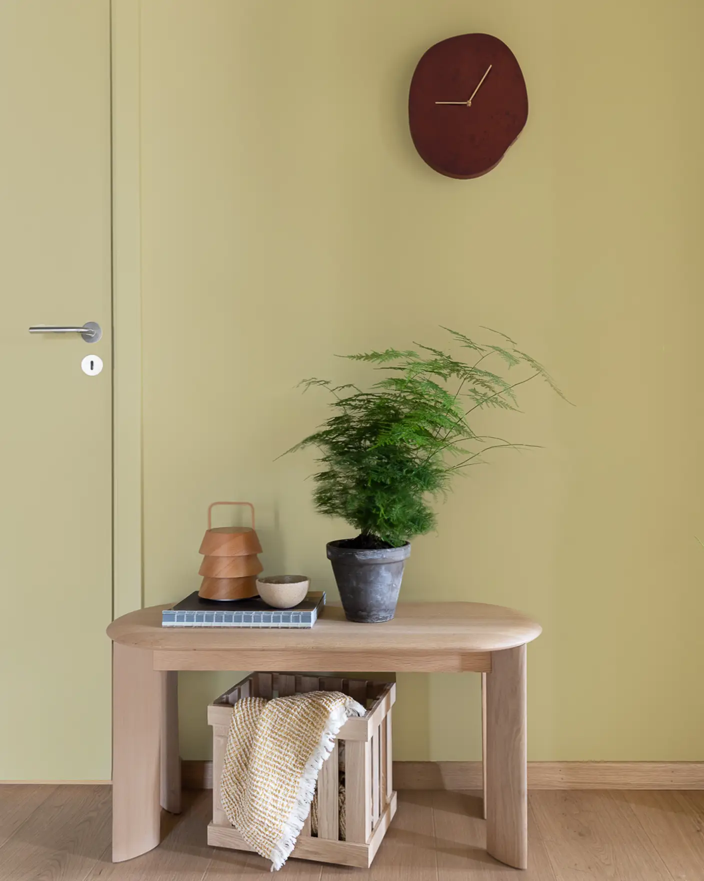 Hallway with bench in oak topped with a green plant, with light green walls painted in JOTUN 8284 Olive.
