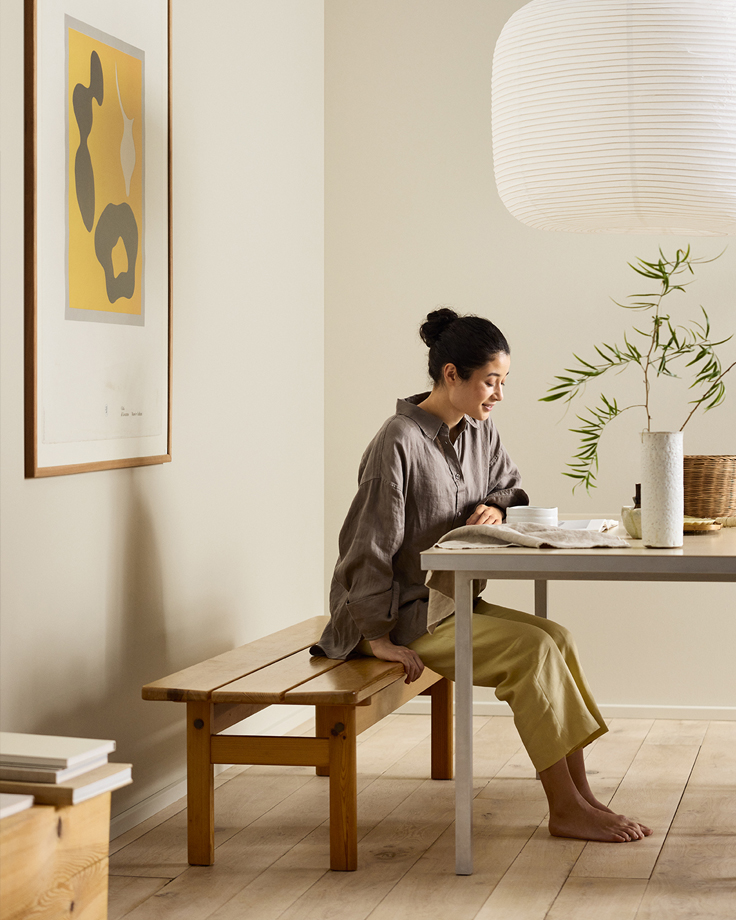 Kvinne sitter ved spisebord og leser, veggene bak er malt i en gyllen beigefarge med Jotun 12308 Unbleached