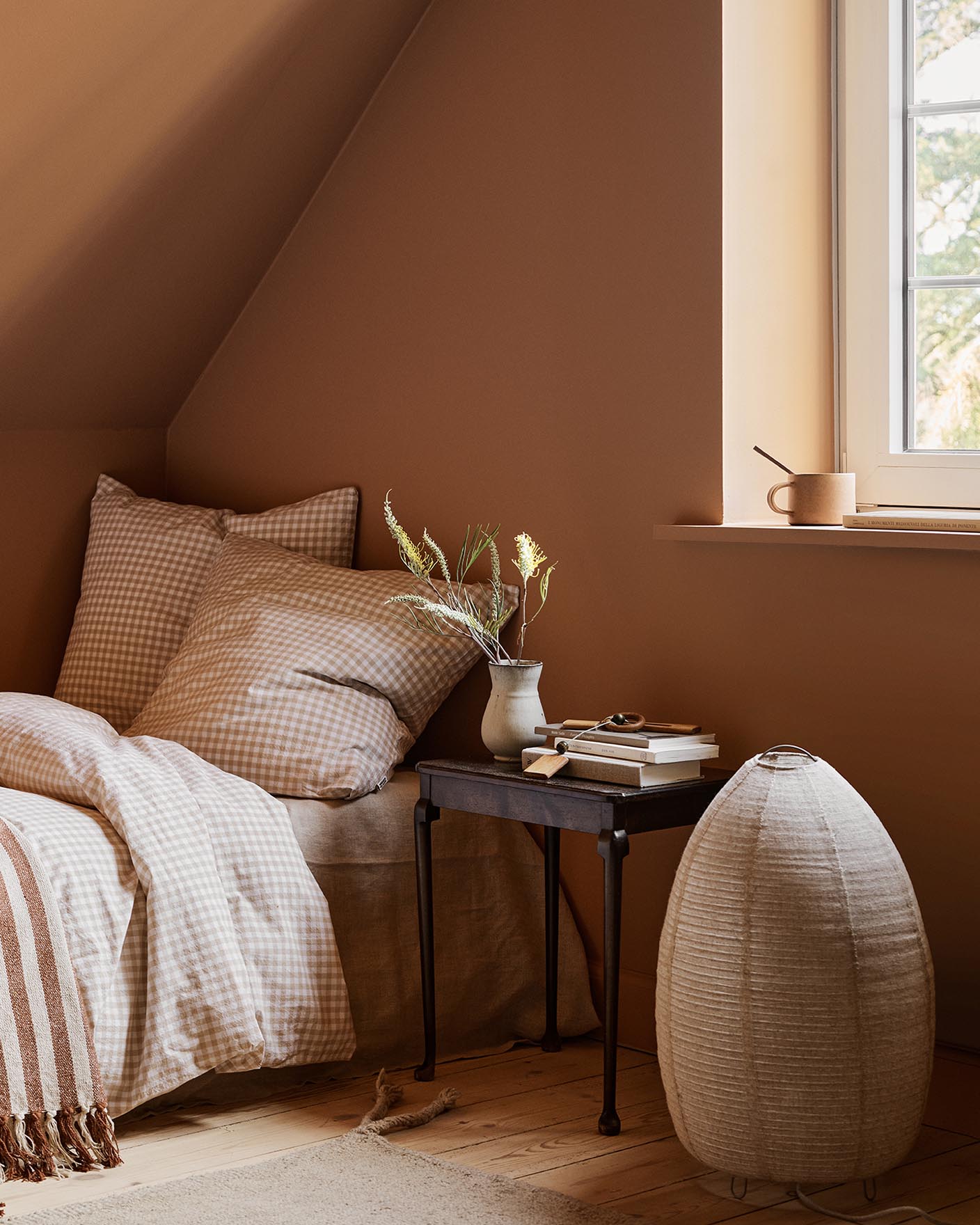 Bedroom with checkered bedding and a black side table against a ochre coloured wall painted with 11220 Ochre Clay from Jotun.