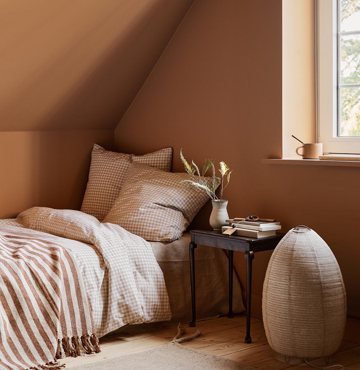 Bedroom with checkered bedding and a black side table against a ochre coloured wall painted with 11220 Ochre Clay from Jotun.