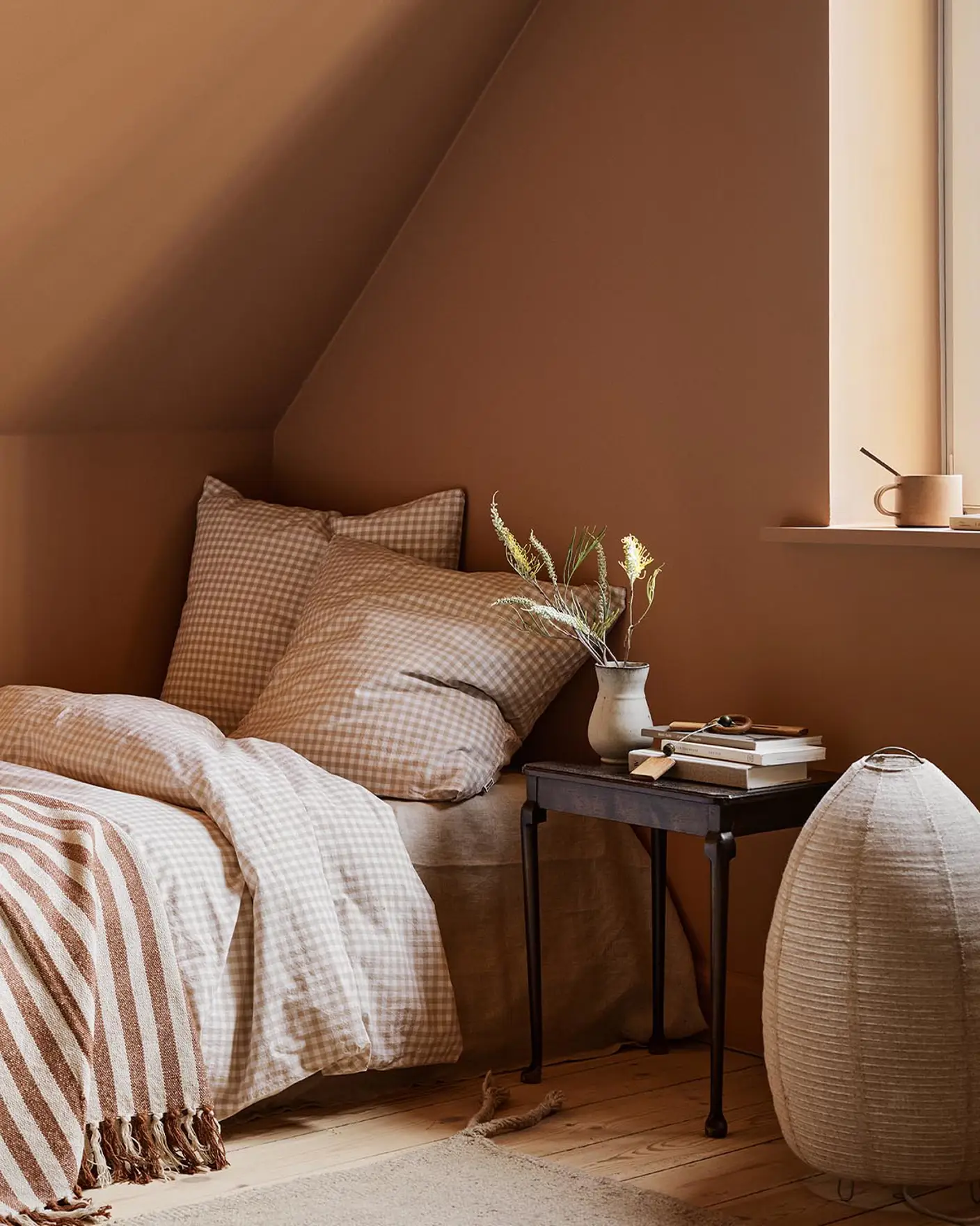 Bedroom with checkered bedding and a black side table against a ochre coloured wall painted with 11220 Ochre Clay from Jotun.