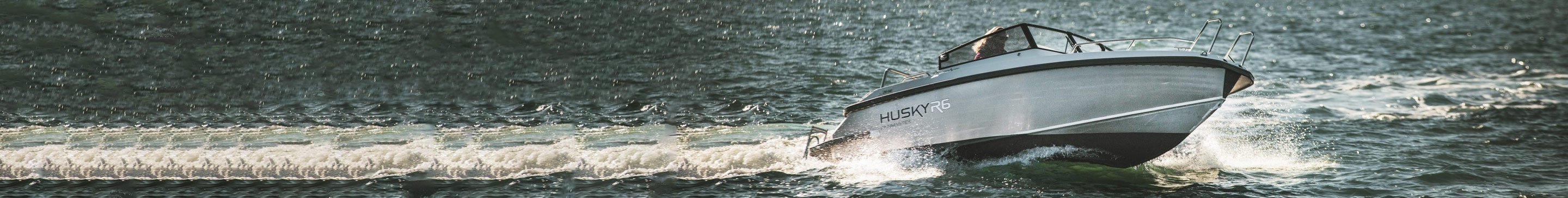 Motorbåt Husky R6 kjører raskt over vannet, lager bølger og skum i kjølvannet