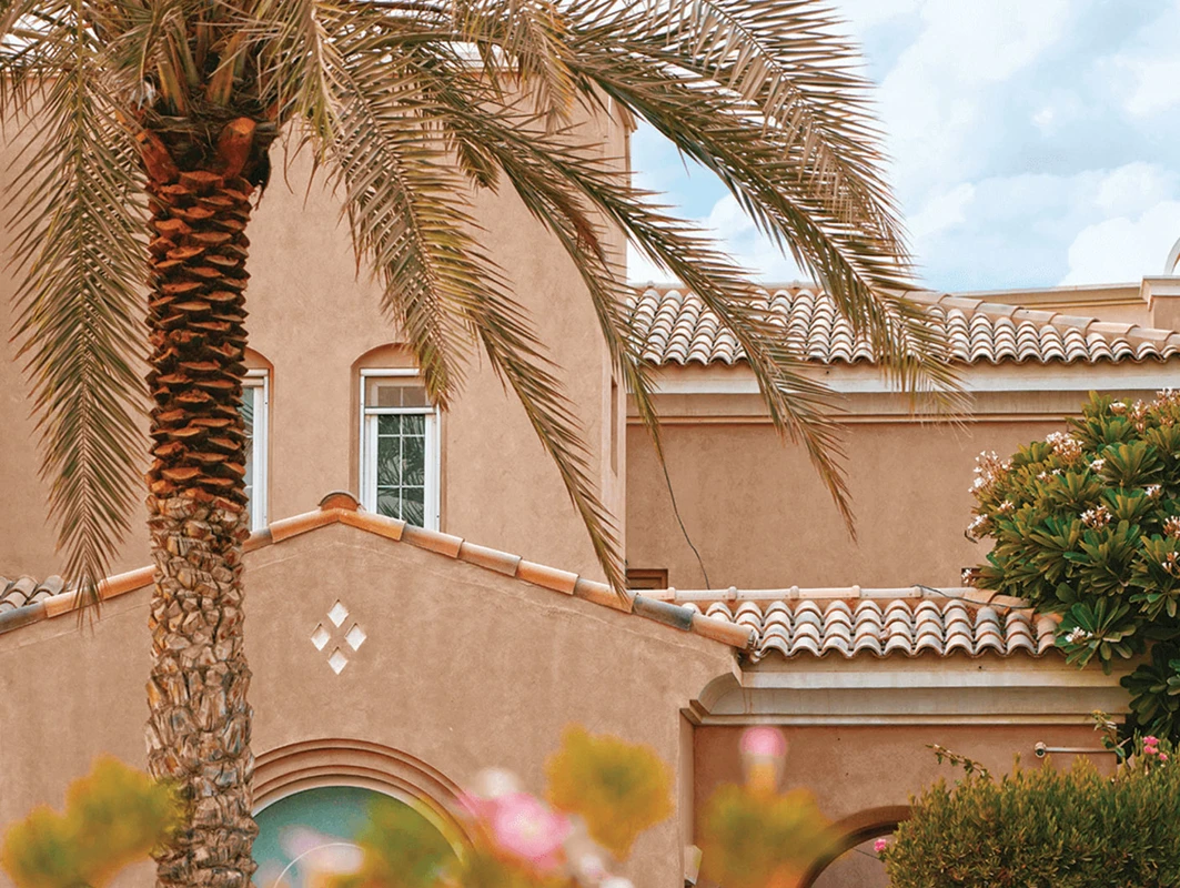 Mediterranean-style house with terracotta roof tiles, surrounded by palm trees and lush greenery
