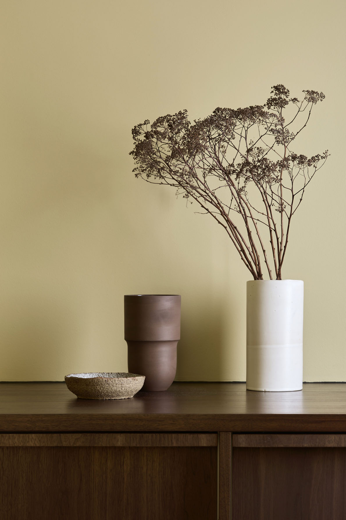 Pottery and a flower vase standing on top of a kitchen cabinet in dark Walnut wood. Walls painted in Jotun Earthy Yellow