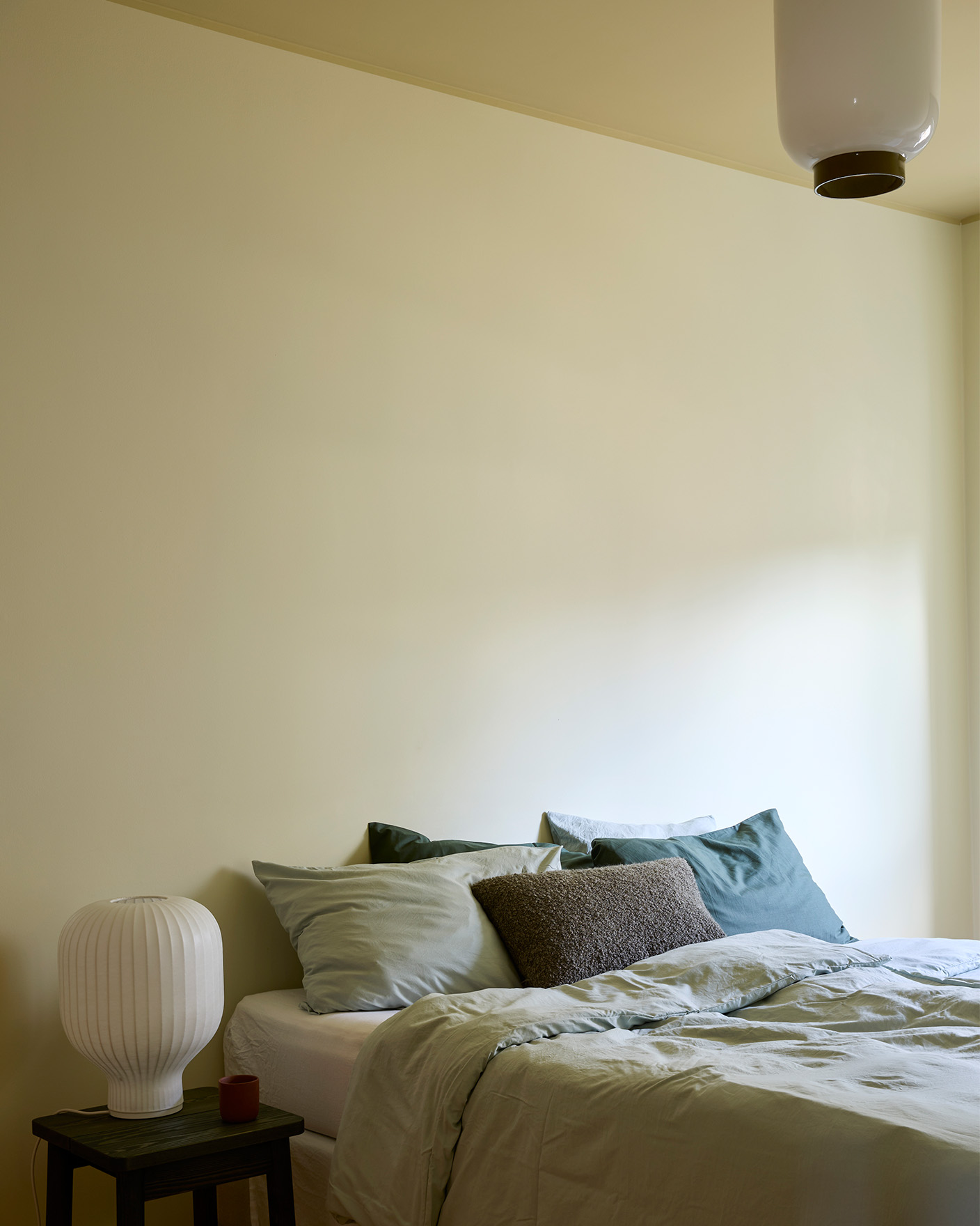 Yellow bedroom painted in the colour Jotun Malmoe and the ceiling painted in Earthy Yellow. Beside the bed is a nightstand with a lamp. 