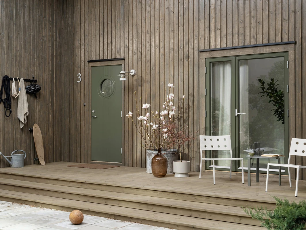 Inngangsparti til et hus beiset med fargen Eldet Grå fra Jotun TREBITT og en dør og vinduer malt i fargen Herregårdsgrønn og trappene er beiset med terrassebeis i fargen Nordisk Tre