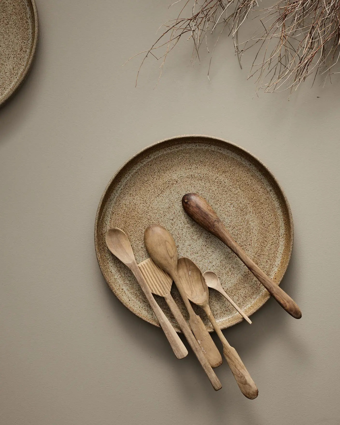 Kjøkkenredskaper av tre på en keramisk plate mot en varm, dempet beige overflate malt i fargen 11130 Shade fra Jotun.